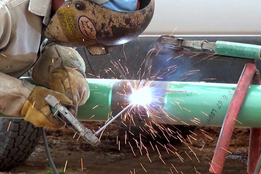 Welder making a weld on coated pipe supported in the ditch