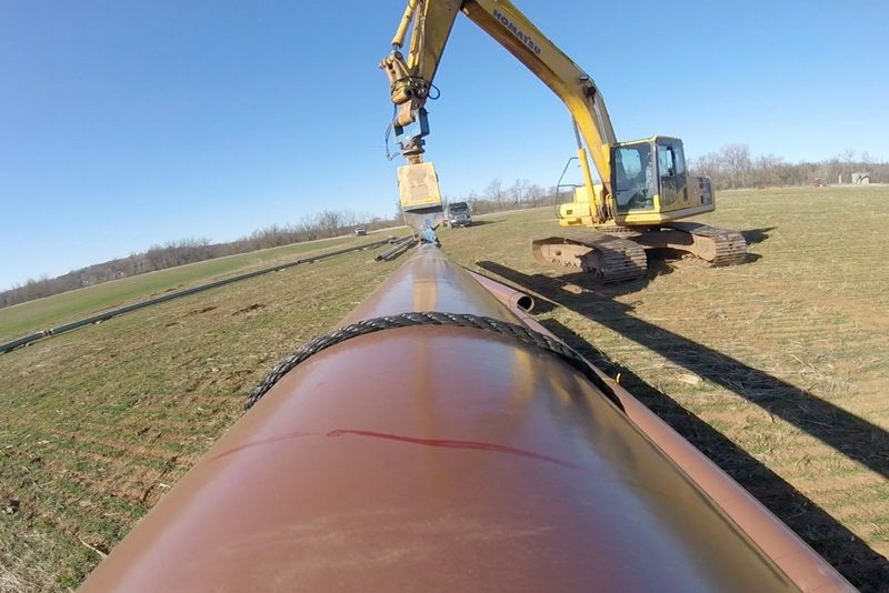 Sideboom and excavator handling a strung pipe section on a Tucker right-of-way