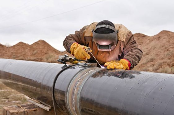 Welder in full protective gear working on a large-diameter pipe